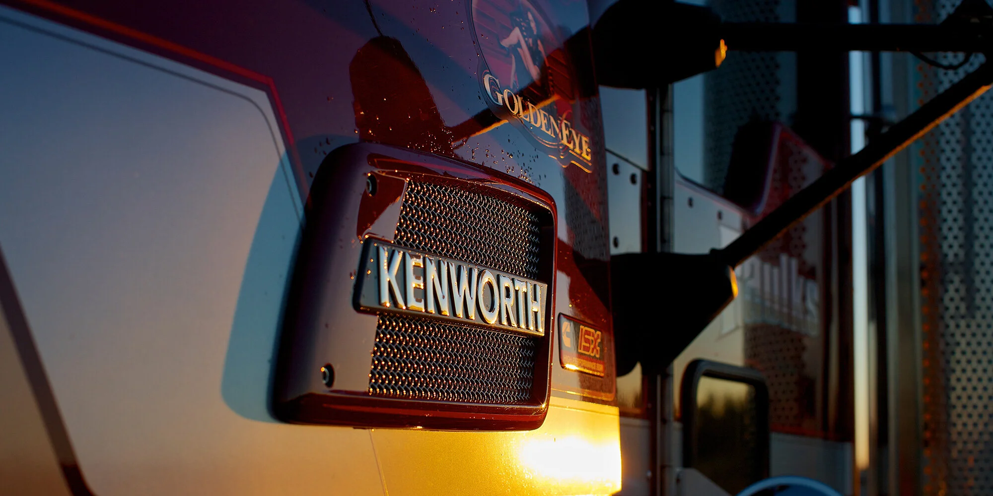 Close-up of a Kenworth truck grille at sunset with the company name illuminated