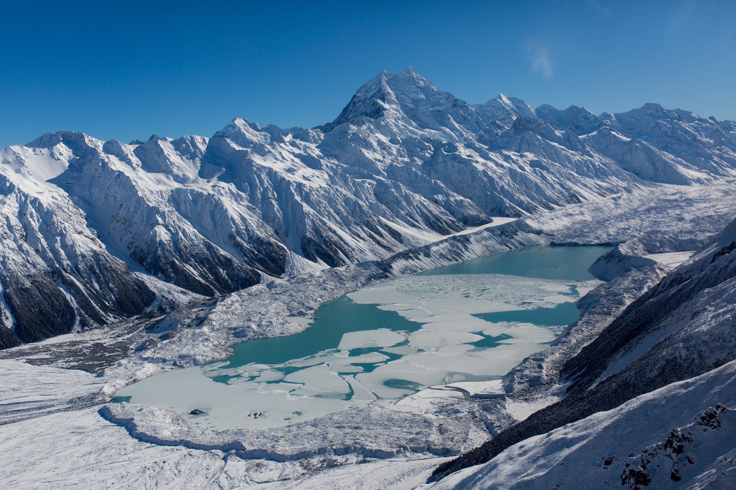 Aerial view over a partly frozen glacial lake beneath Aoraki Mount Cook in winter