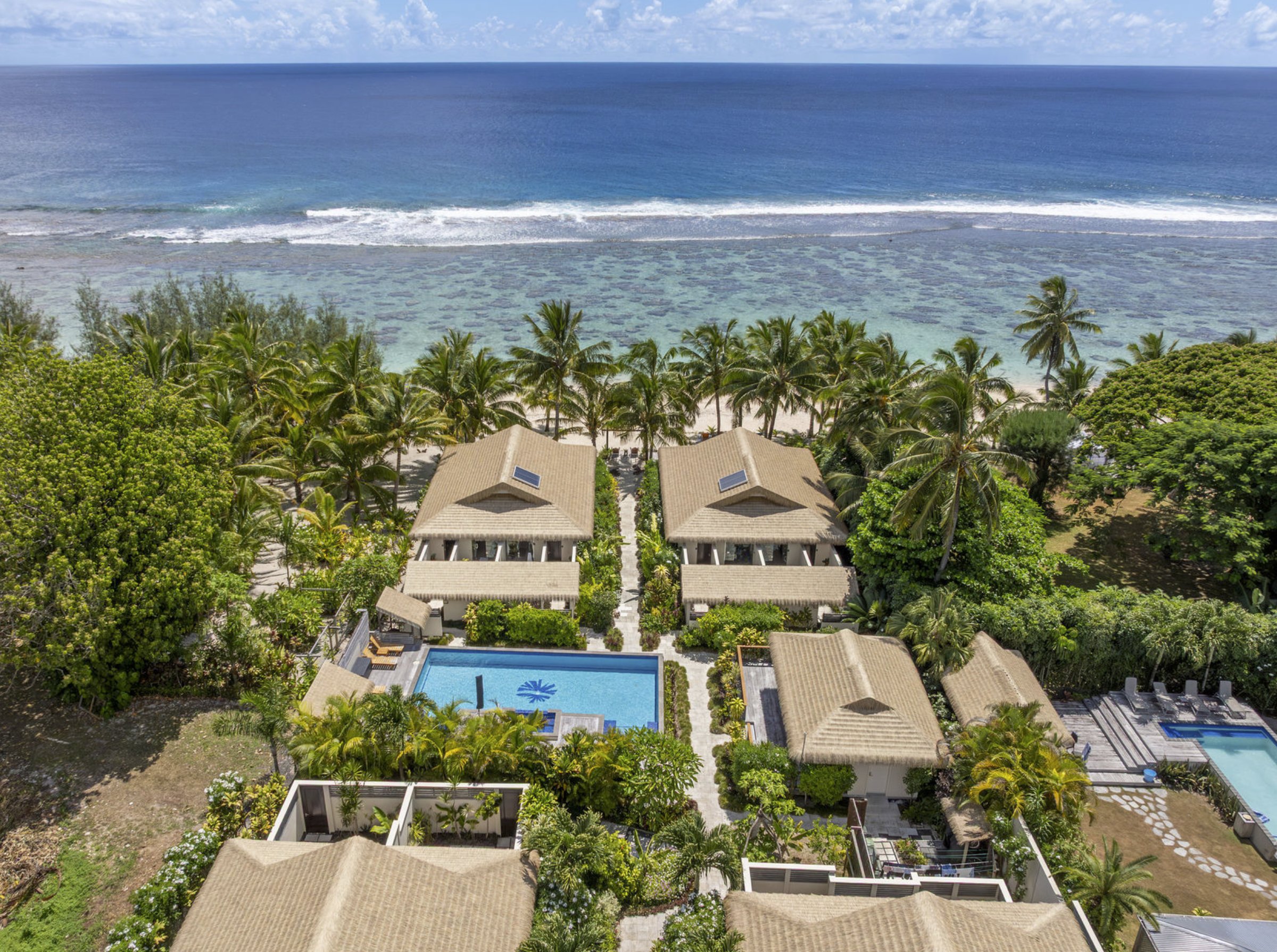 Aerial view of a thatched-roof beachfront resort beside a coral reef lagoon