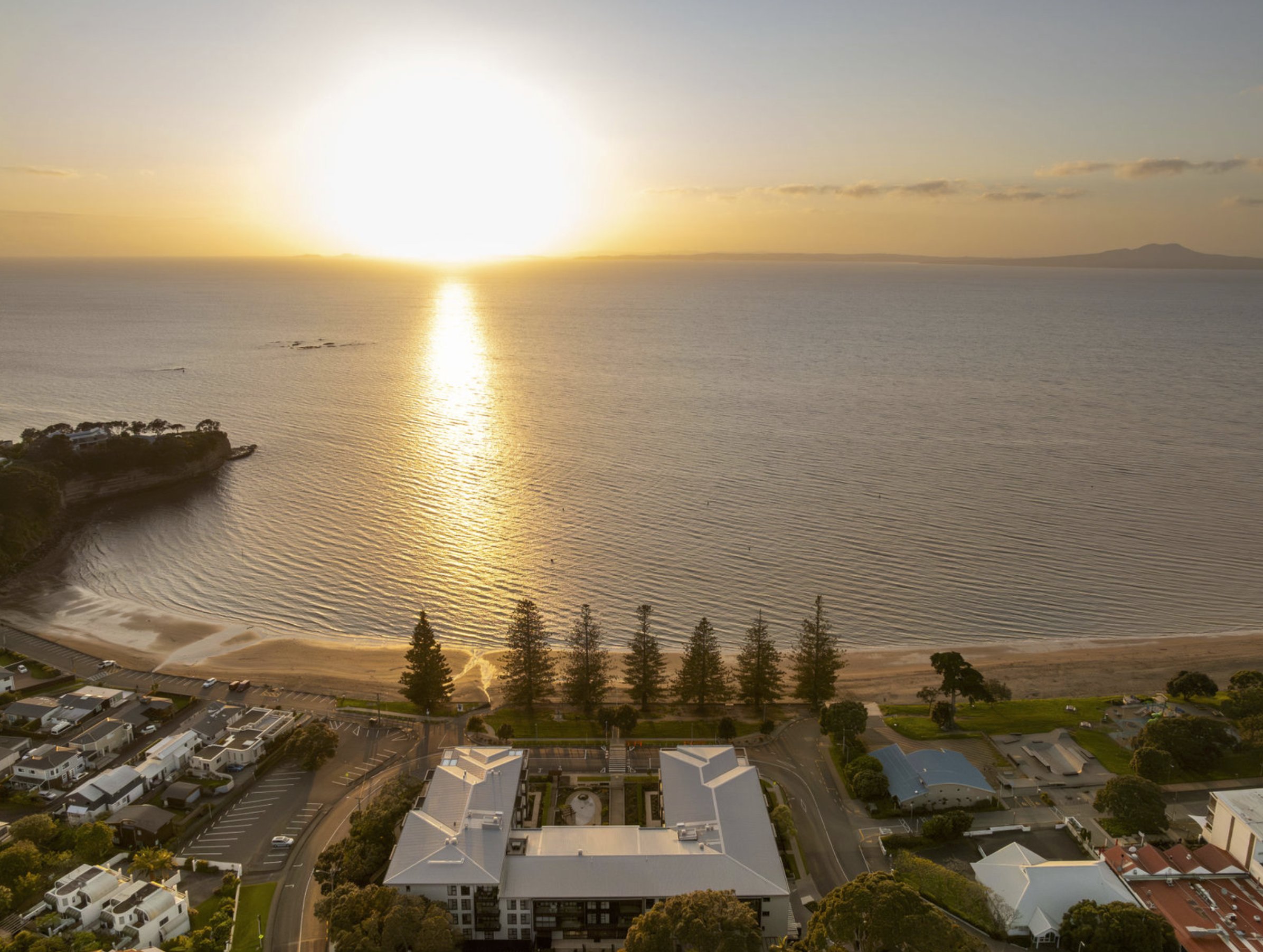 Aerial view of a coastal apartment development at sunrise, with the sun reflecting off the sea