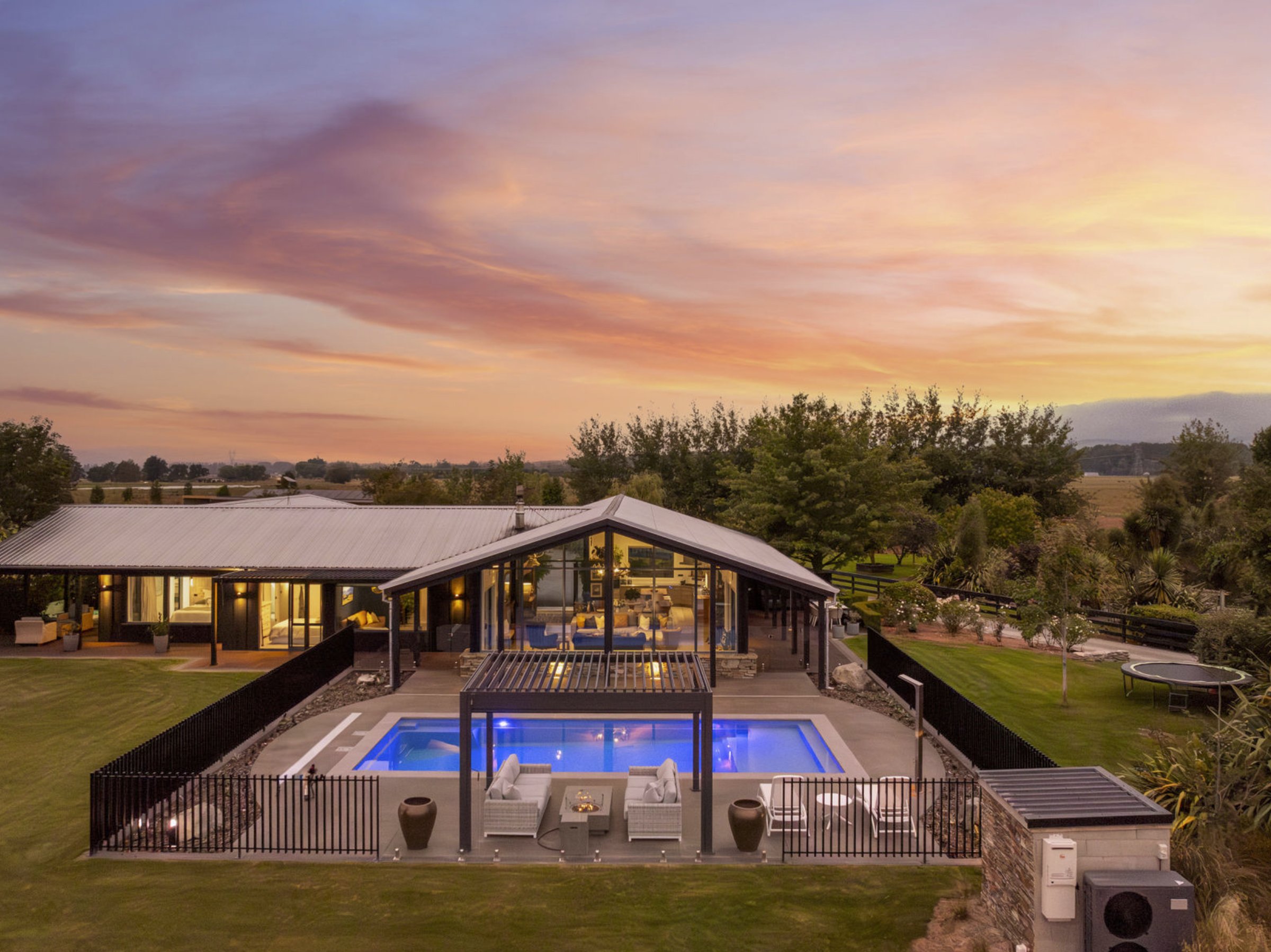 Aerial view of an architecturally designed rural home with a lit swimming pool at dusk