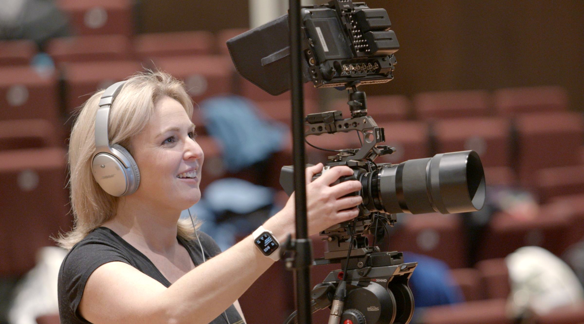 Camera operator smiling behind a cinema camera rig during a theatre production