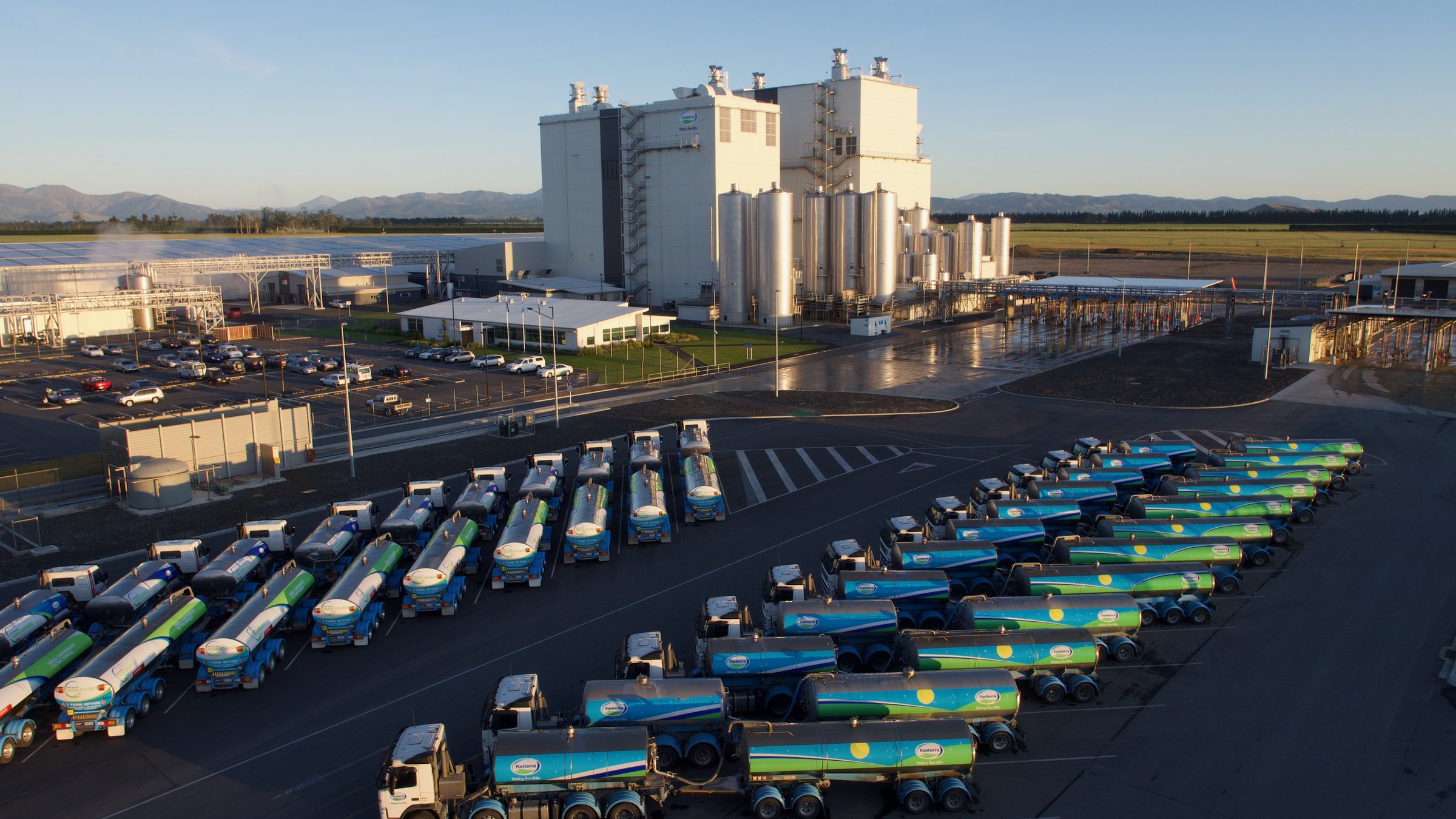 Aerial view of a Canterbury dairy processing plant with rows of milk tankers at dawn