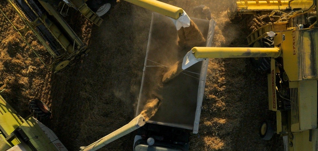 Overhead drone view of combine harvesters unloading grain into a truck at harvest